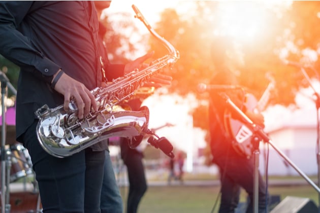Photograph of a saxophonist performing outdoors in a park setting.