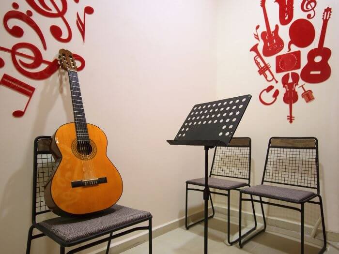 Acoustic guitar and sheet music stand next to some chairs in an empty music classroom.