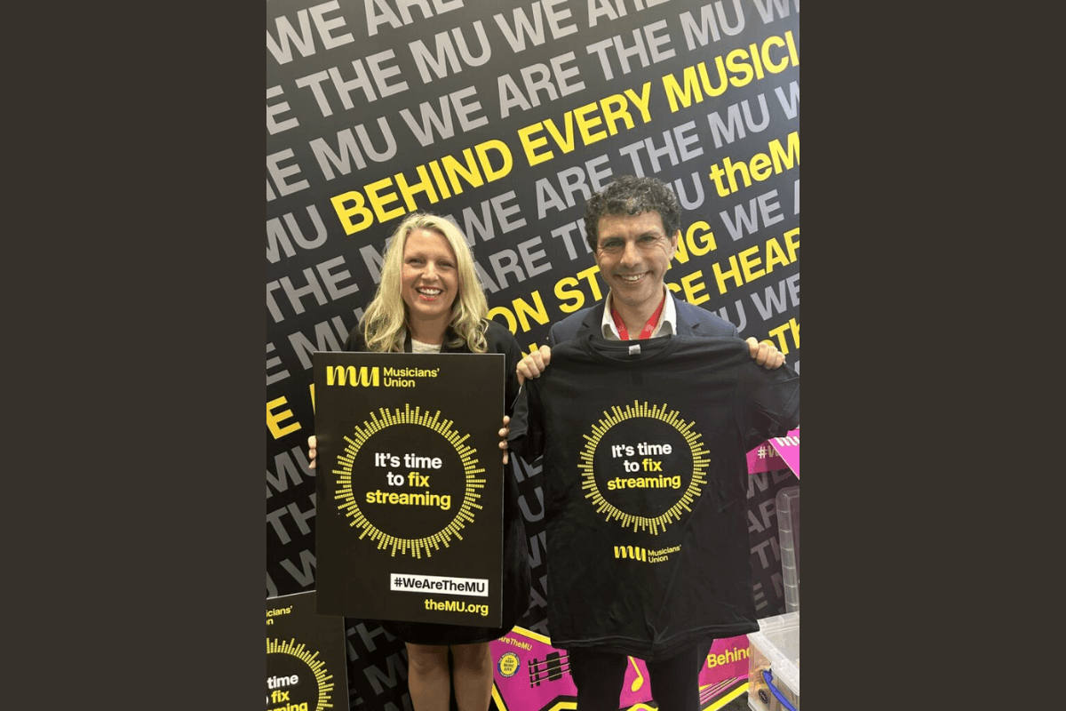 Naomi Pohl and Alex Sobel MP holding black t-shirts that say in yellow “It’s time to fix streaming’. In front of a Musicians' Union stand at Labour Party Conference 2024.