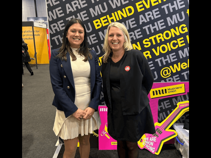 Lisa and Naomi on the MU's stand at Labour Party Conference in 2024, they are against a black and yellow backdrop that says 'We are the MU' and 'We are Union strong'.