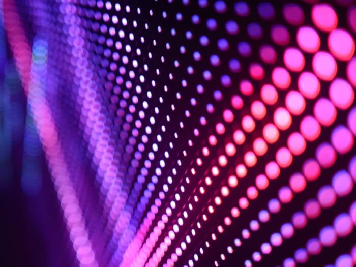 Bright abstract neon dots are blurred in dark space, in pink and purple colours with a party like atomosphere