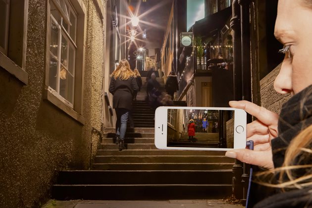 A woman holding a phone with the footage of people walking on street stairs in Edinburgh