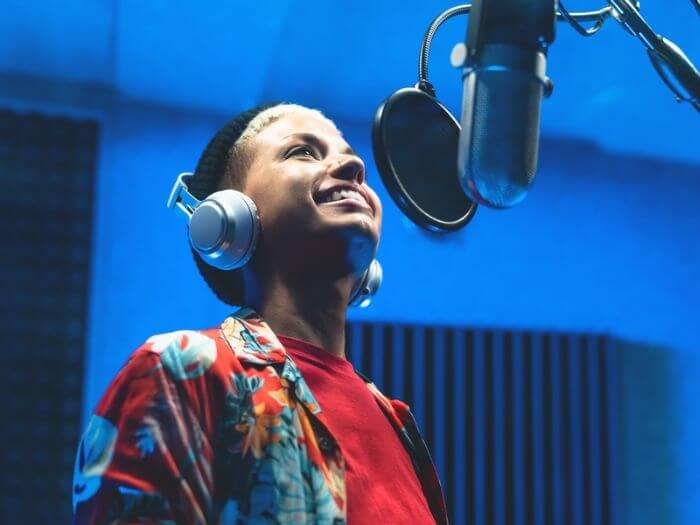 Young musician in a recording studio, smiling as they sing into a mic with pop shield.