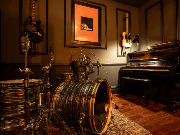 Photo of a warmly-lit recording studio with a drum kit and piano.