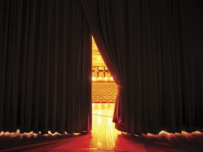 Stage curtains opened a crack, showing theatre and lights behind.