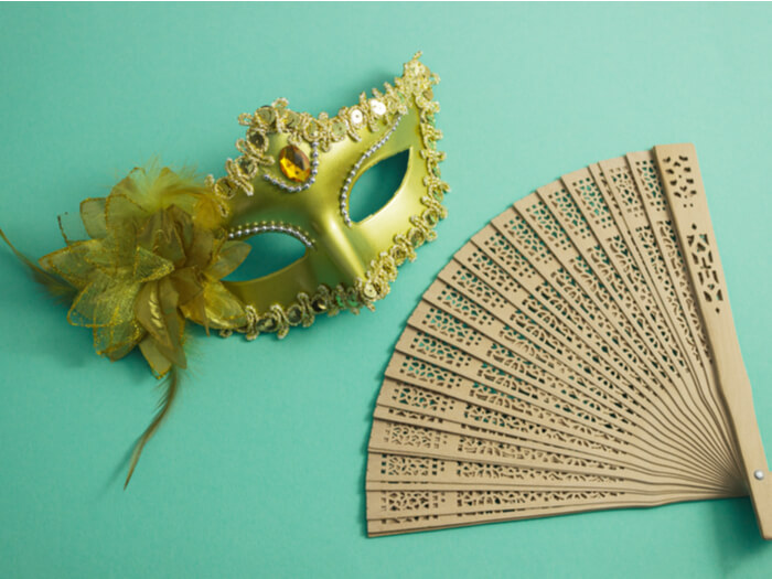 Golden opera mask and a white wooden fan on a bright turquoise background