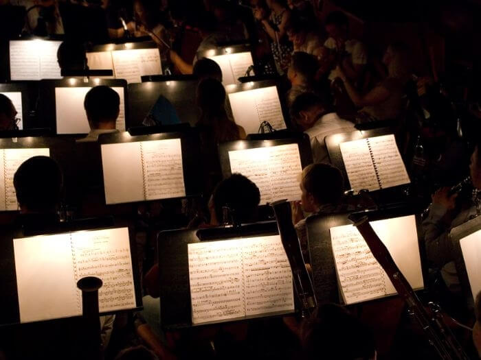 Darkly lit orchestra pit with musicians and music sheets.