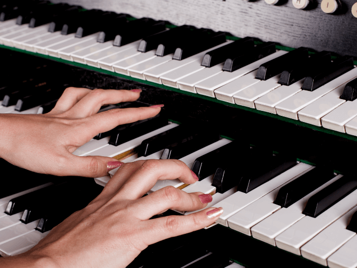 Organist with painted nails playing a pipe organ, closeup view of hands and keys.