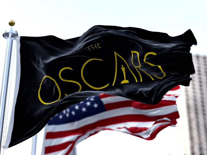 Flag with the Academy Awards logo waving with the American flag blurred in the background.