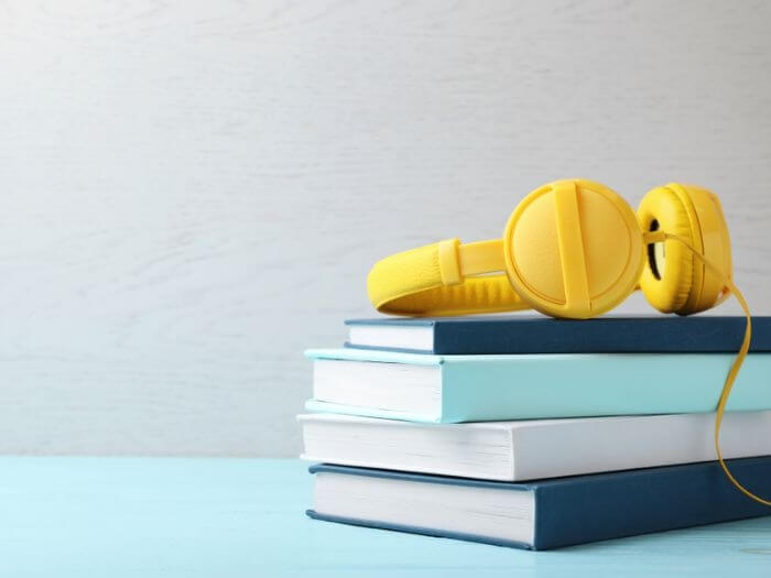 Yellow headphones on the top of a pile of stacked, blue hardback books.
