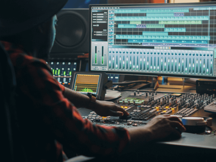 Black music creator sat at mixing desk/laptop in a recording studio.