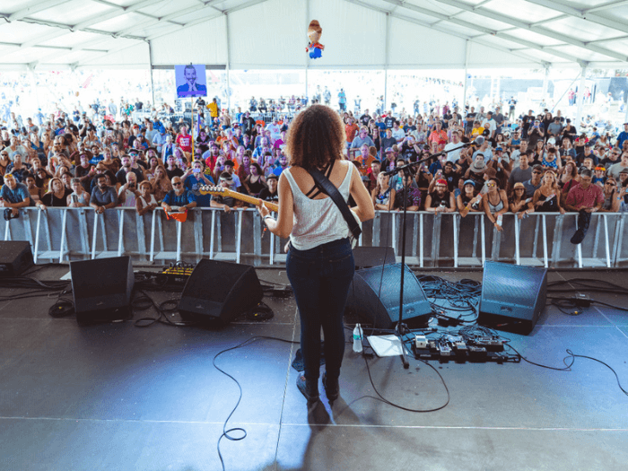 A female musician with a guitar performing at a festival to a crowd in Austin, Texas.