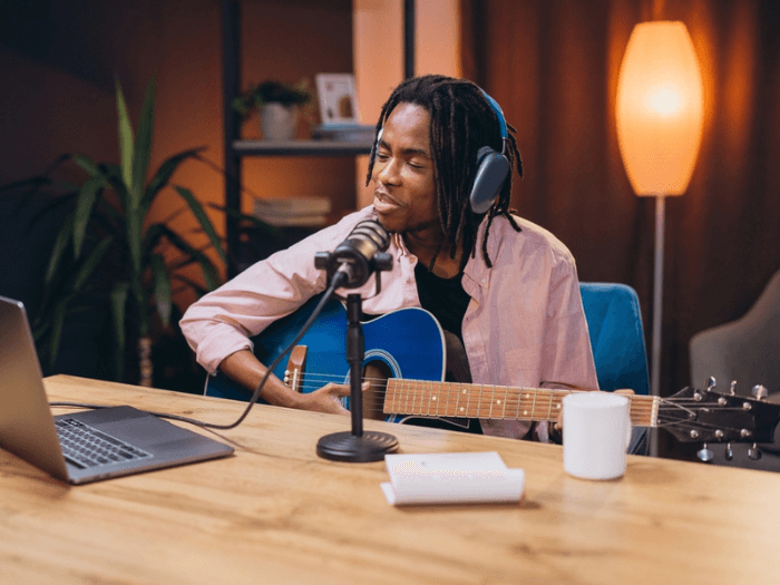 A musician playing guitar and singing into a microphone in a compact home studio.