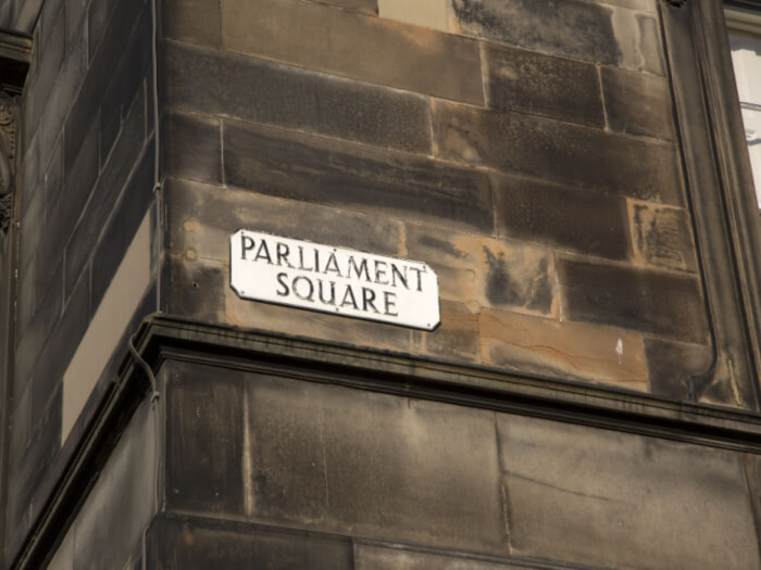 The tall corner of a building on Parliament Square with a street sign on it reading 