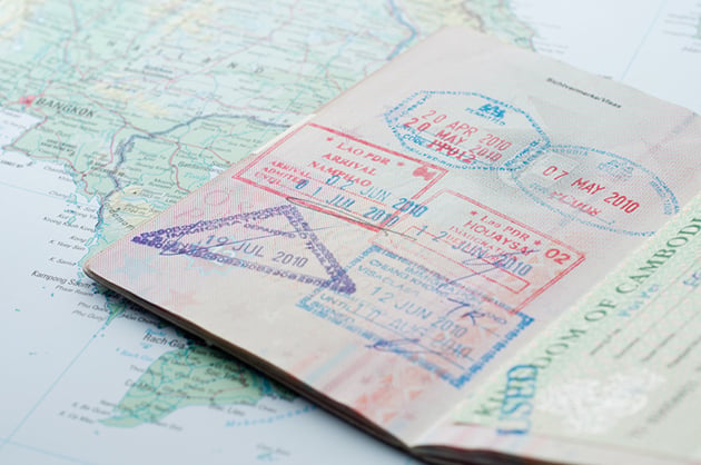 Open passport showing country stamps, lying over a map of the world.