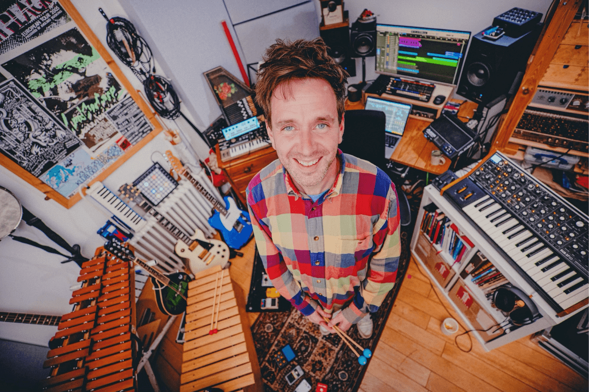 Paul Russell smiling in his studio, surrounded by instruments.