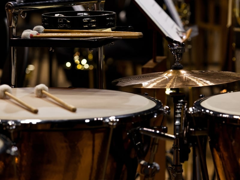 Two sets of drum sticks lie on different instruments in a percussion section set up but with absent musicians.