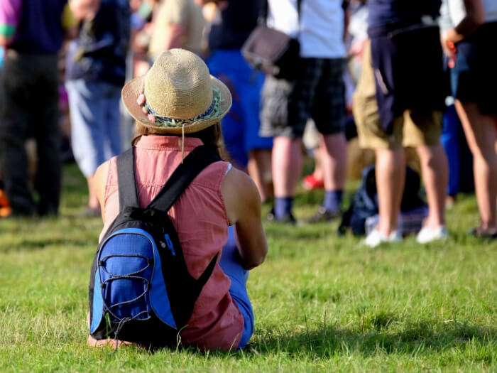 Person sits on the grass amongst a crowd of festival goers in the sunshine.
