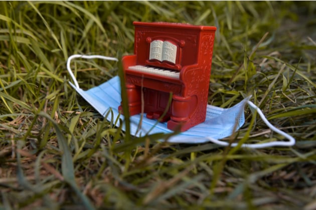 Photograph of a tiny model piano, placed outside and resting on top of a face mask.