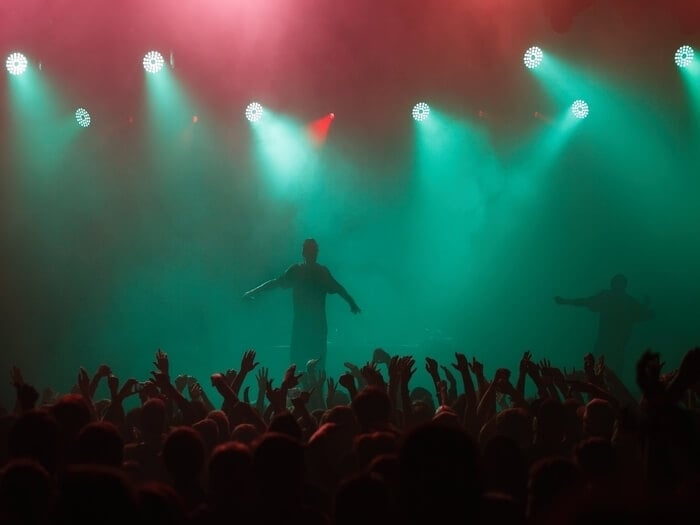 A musician standing on a stage at a festival with audience members waving their hands.