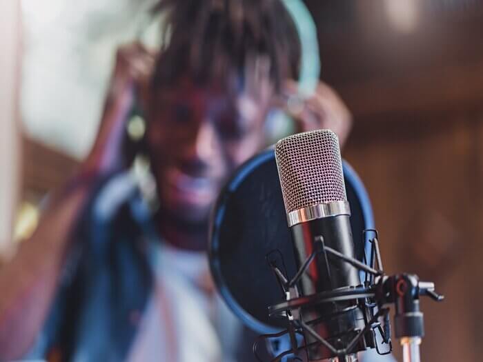Young Black musician, wearing headphones, In the foreground is a recording mic and pop shield.