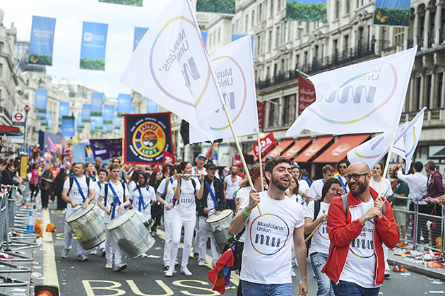 Marching band wearing t-shirts with Musicians' Union equality logo print, and waving flags