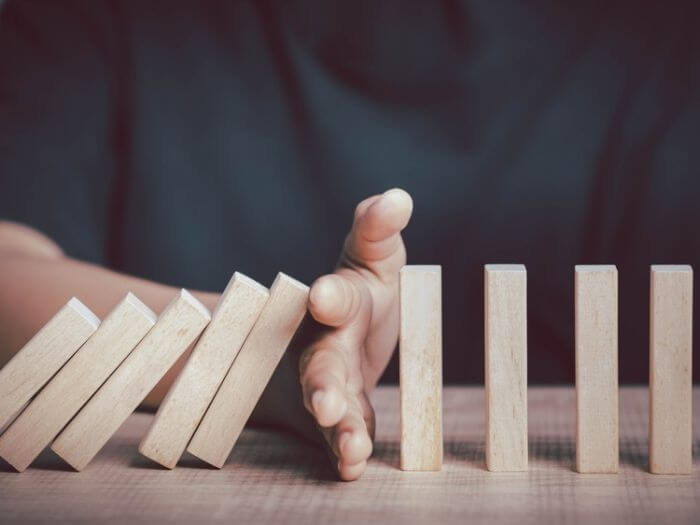 Hand stopping wooden dominos from falling, a proactive concept.