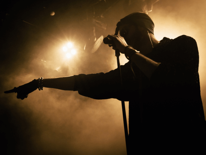 Close up of young, Black male musician, singing into a microphone on a stage.