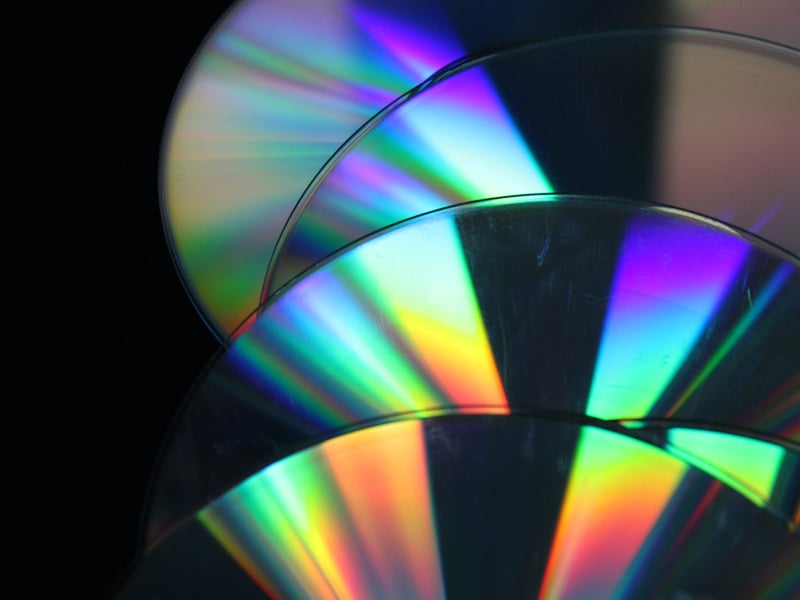 Close up of pile of CDs, showing rainbow colours in the refraction of the light.