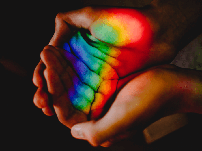 Cupped hands holding the light of a rainbow.