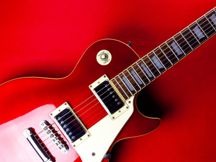 Red vintage guitar against a red background.