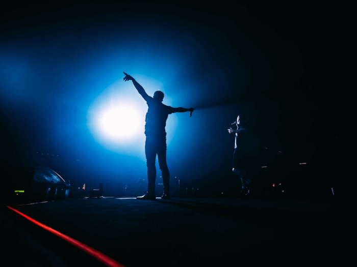 Silhouette of male singer on stage in front of a blue light, holding his hands out to the crowd.