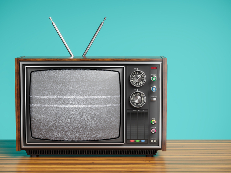 Photograph of a retro television set in front of a turquoise background, showing fuzz on the screen.