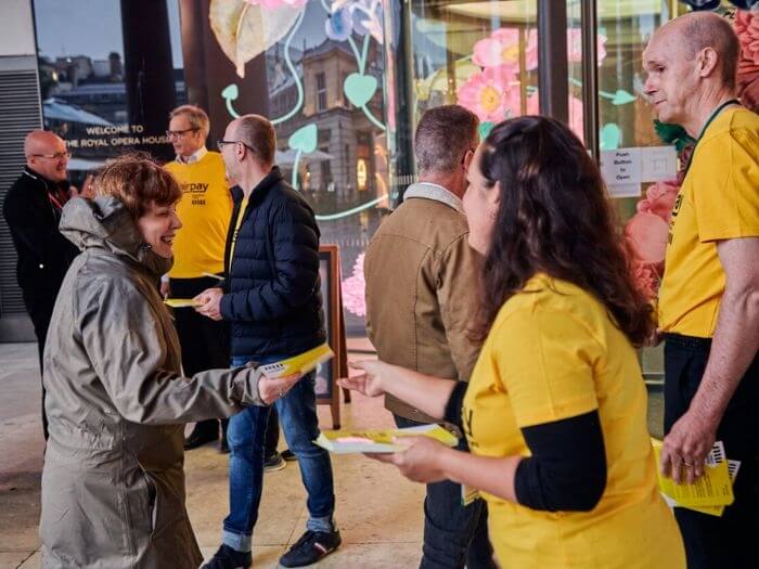 Members of the Royal Opera House Orchestra dressed in their yellow #fairpay t-shirts handing leaflets to audience members as they arrive for the performance.