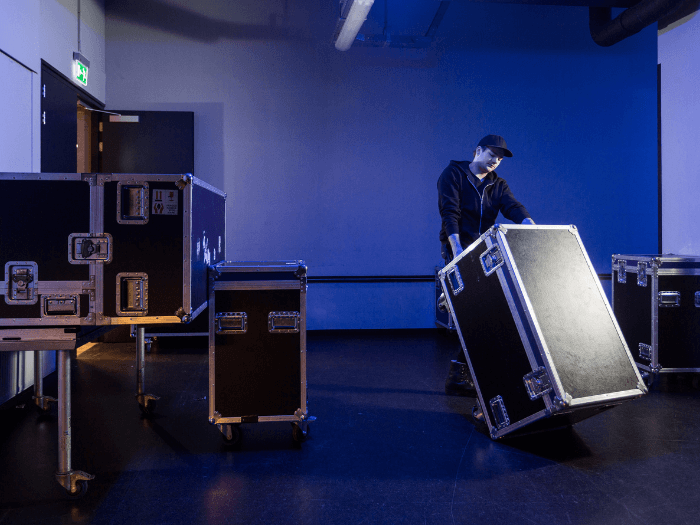 Roadie tipping a flightcase over on it's side in a room of other storage boxes.