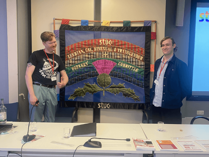 Andrew Collings and Duncan McBride standing in front of an STUC LGBT+ tapestry before conference.