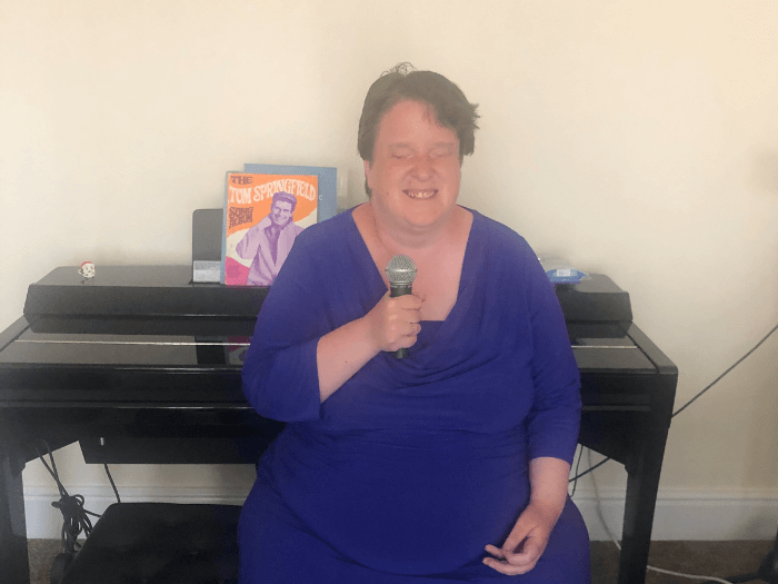 Professional singer Sarah Mellor sitting at a piano holding a vocal microphone.