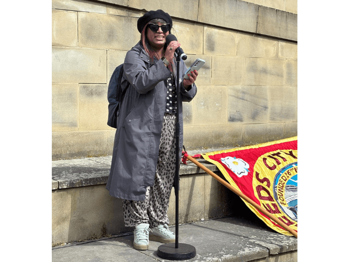 Sashwati reading notes from her phone while speaking into a microphone on stone steps.