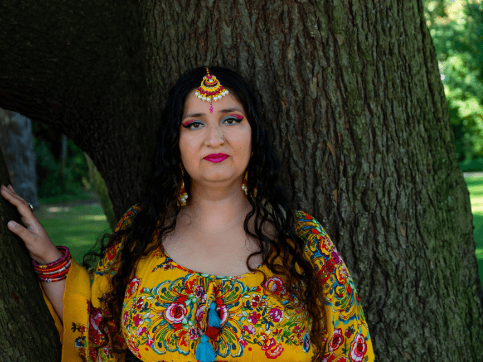 Folk singer-songwriter Satnam Galsian standing in front of a tree and wearing bright clothes and jewellery.