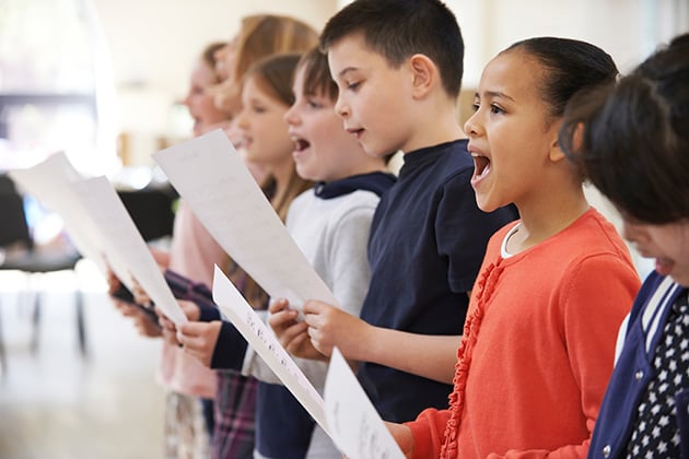 Photograph of a group of children singing in a school classroom setting. Photo credit: Shutterstock