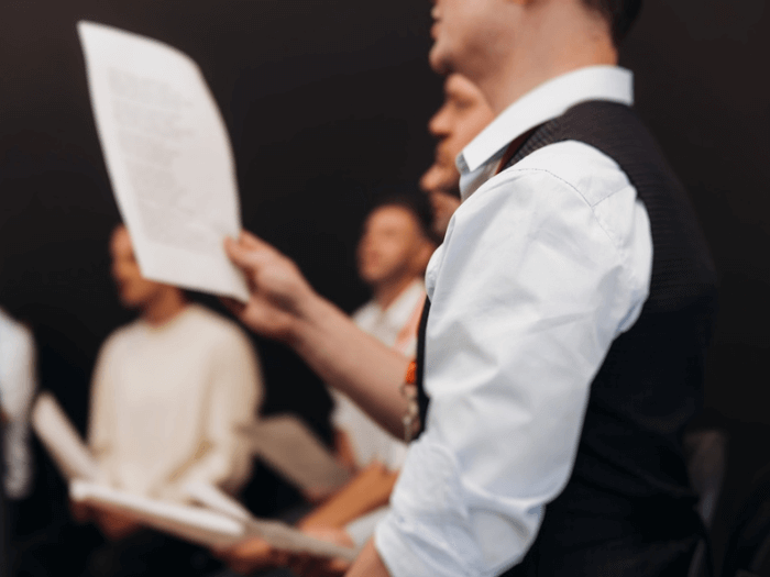 Professional singers rehearsing on stage holding sheet music.