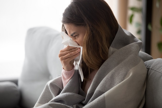 Photograph of woman sneezing into a tissue.
