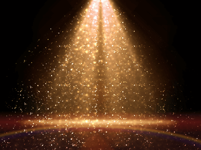 Golden glitter and confetti caught in a spotlight on stage.