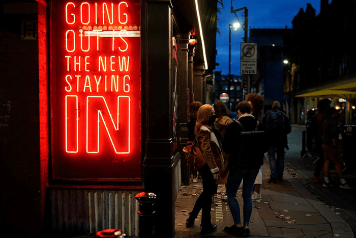 Side view of Manchester bar at the nighttime with red neon sign saying 'Going out is the new staying in' after lockdown restirctions were eased last year.