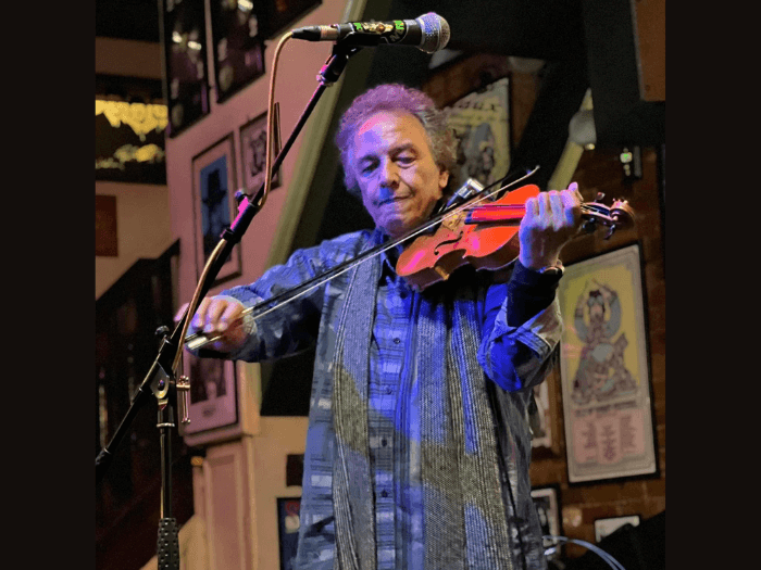 Steve playing fiddle live in front of a microphone on a stand.