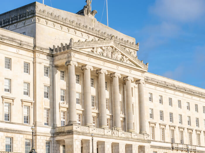 The sun shines on the outside of the Stormont building under a blue sky.