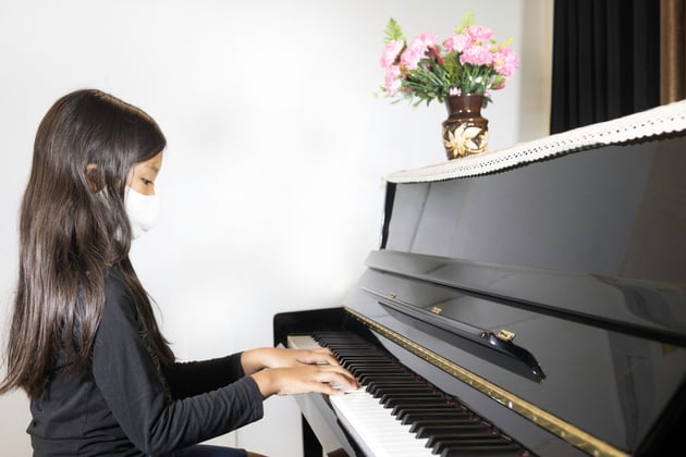 Photo of a young student wearing a mask while playing piano.