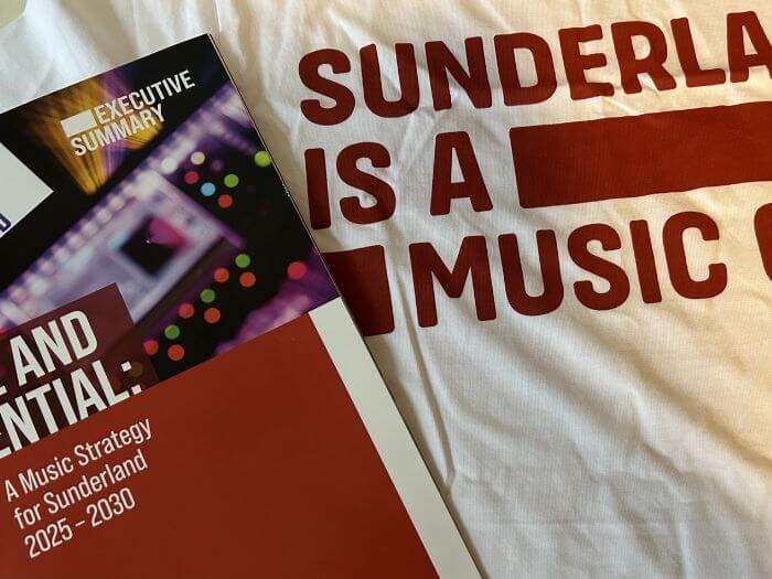 Close up of a white t-shirt with red writing saying “Sunderland is a music city”, next to a leaflet saying “A music strategy for Sunderland 2025-2030”.