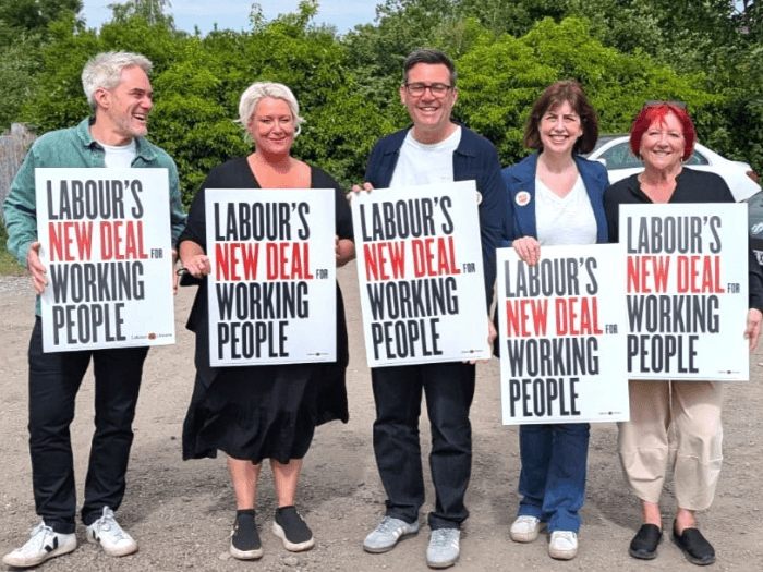 Four people, including MU Assistant General Secretary Matt Wanstall and Andy Burnham, holding signs saying 