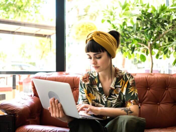 Young women sat at an open laptop in a brightly lit cafe.